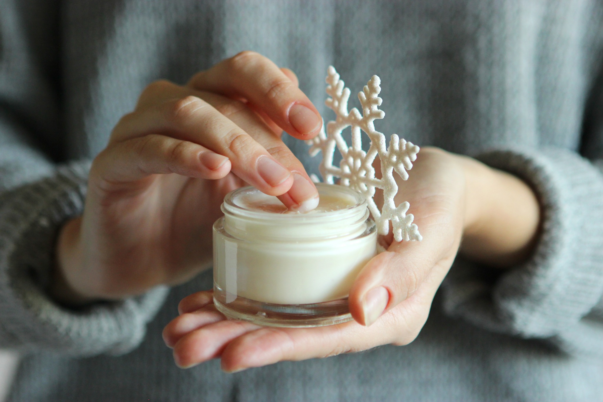Image of woman's hands holding moisturizer and a snowflake to give concept of dry winter skin