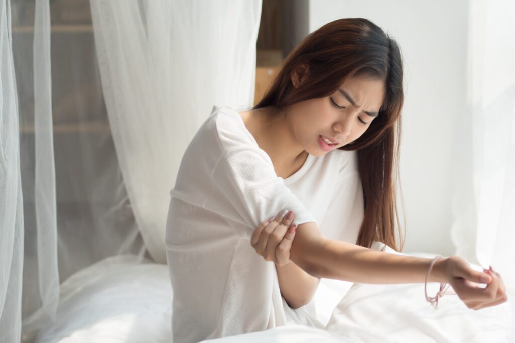 Woman Sitting In Bed, Holding Her Arm In Pain