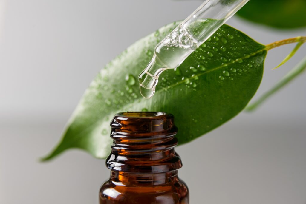 Image Of Amber Bottle Of Serum With A Green Leaf In The Background.