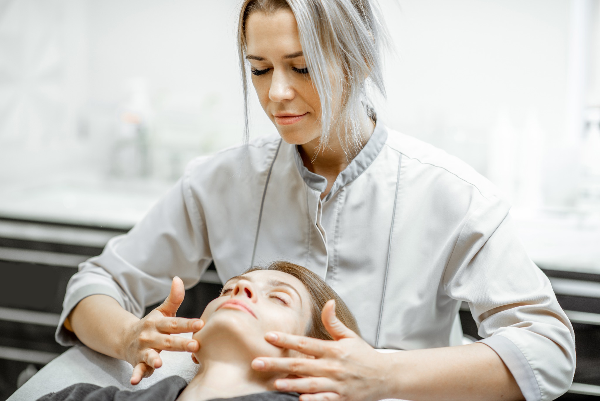 Image of a female massage therapist finishing a facial massage on a client